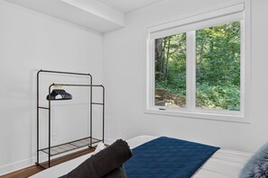 A room with a bed, a window with a forest view, and a metal drying rack. - Bellaria Tremblant - Private villa with SPA (Mont-Tremblant)