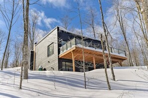A modern cabin with a wooden deck, large windows, and a snowy landscape. - Bellaria Tremblant - Private villa with SPA (Mont-Tremblant)