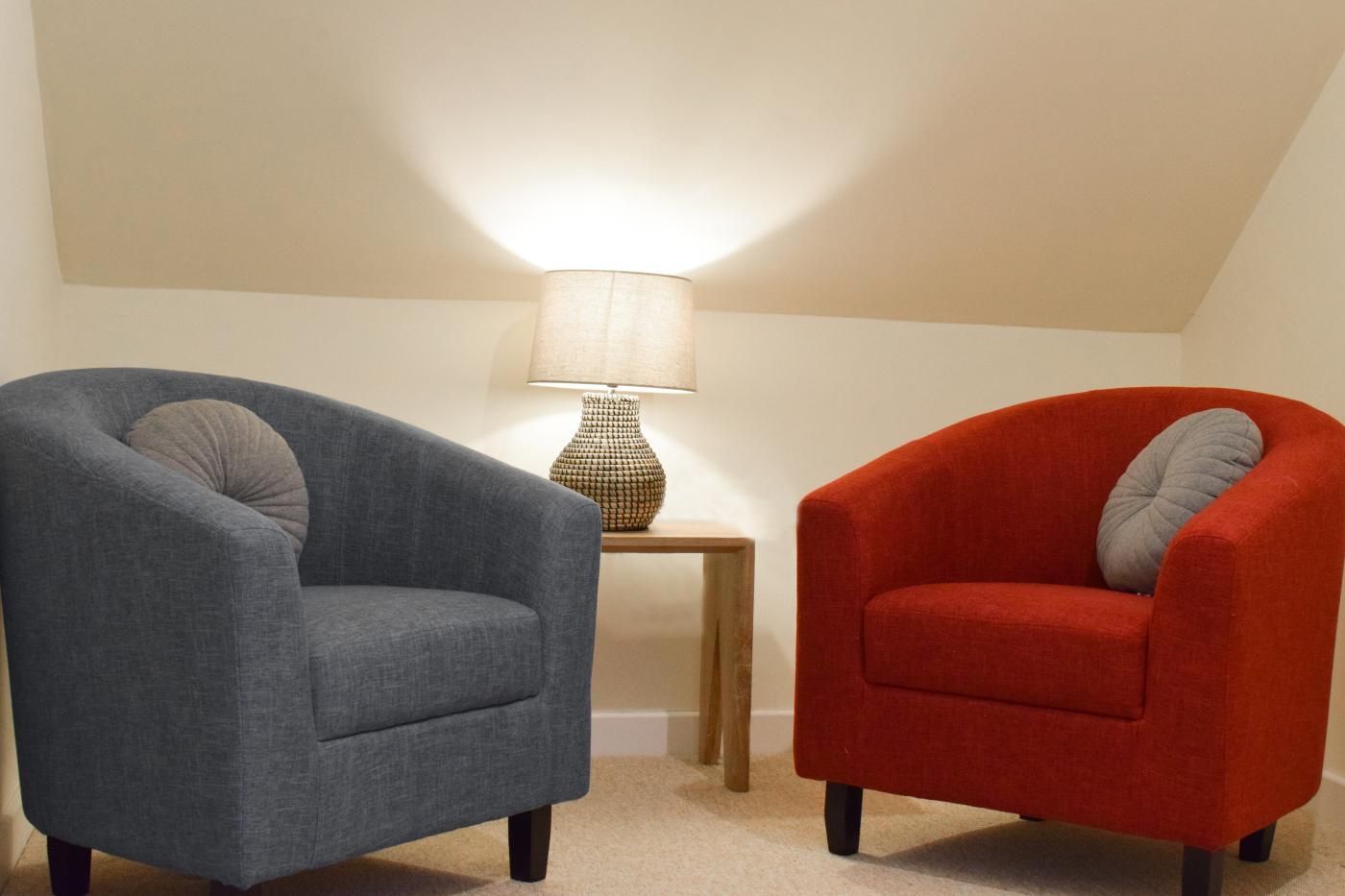 Two armchairs, one grey and one red, with a lamp on a small table between them.
