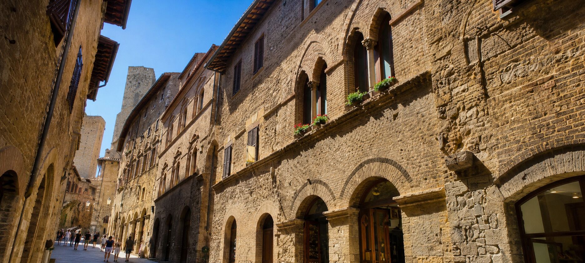 A narrow street lined with historic stone buildings, featuring arched windows and doorways, and a clear blue sky above.