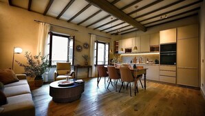 Ein modernes Wohnzimmer mit Sofa, Couchtisch und Essbereich mit Stühlen. Es gibt eine Küche mit Schränken und Geräten.