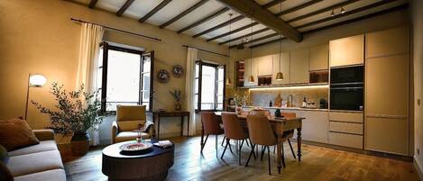 A modern living room with a sofa, coffee table, and dining area with chairs. There is a kitchen with cabinets and appliances.