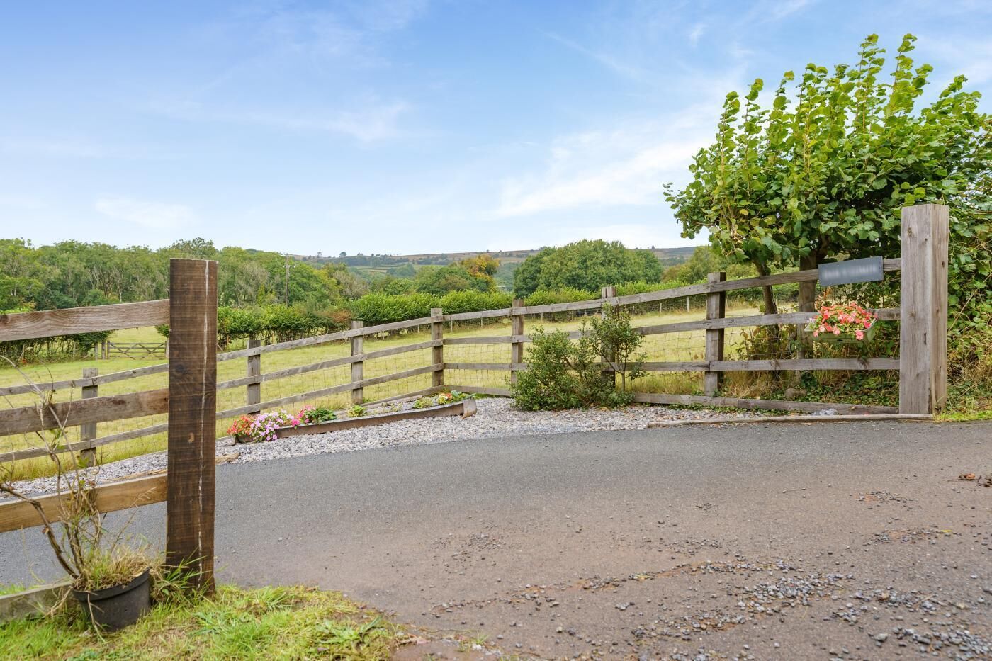 A rural landscape with a wooden gate, gravel path, and a fence.