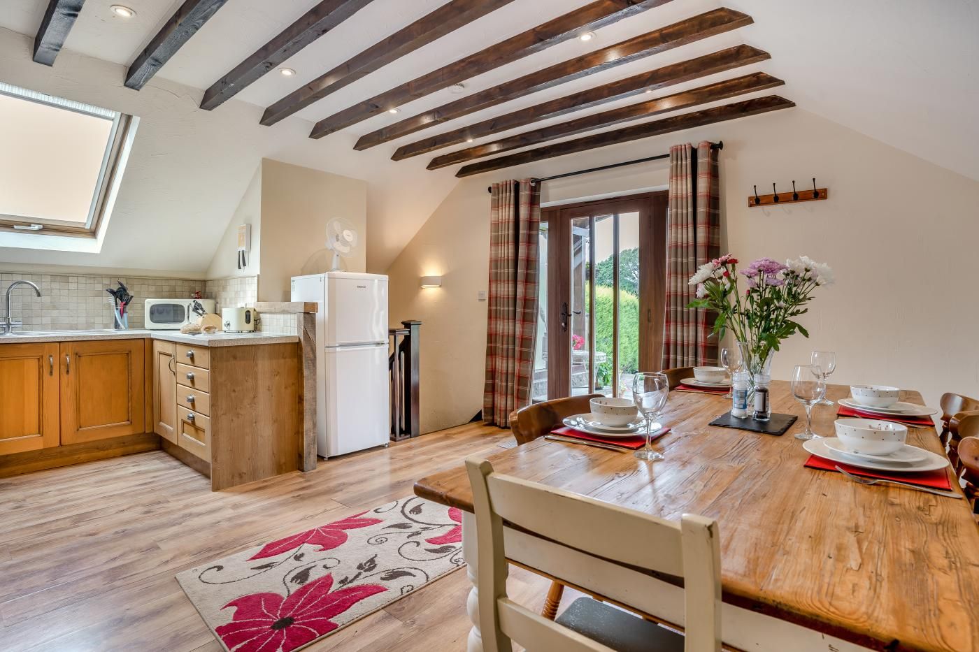 Une cuisine moderne avec des meubles en bois, un réfrigérateur et un coin repas avec une table mise pour deux personnes.
