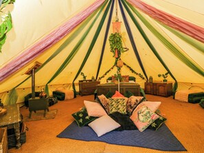 A tent interior with a bed, pillows, a hanging plant, and a small table. - Jungle Bell Tent (Newbury)