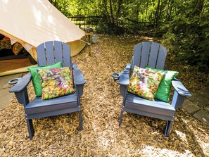Two Adirondack chairs with colorful cushions, a tent, and a forested background. - Jungle Bell Tent (Newbury)