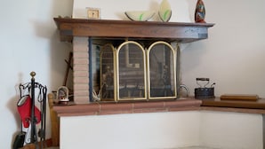 A corner of a room with a fireplace, a broom, a red oven mitt, and a small table with a clock. - Lavanda Apartment – Ultra-fast WiFi & Workspace in Valdarno (Pestello)