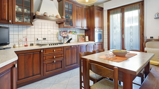 A kitchen with wooden cabinets, a stove, and a dining area with a table and chairs. - Lavanda Apartment – Ultra-fast WiFi & Workspace in Valdarno (Pestello)