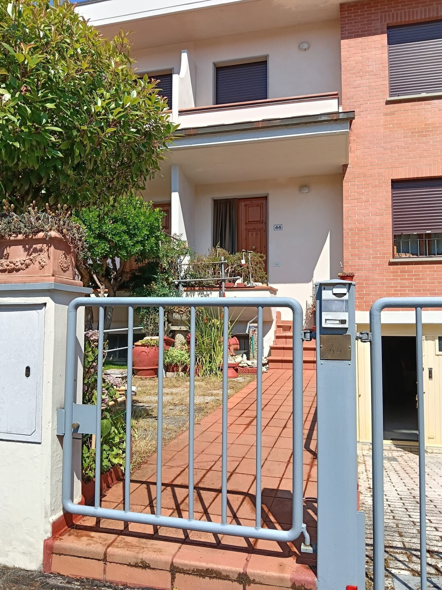 Ein begrenzter Zugang zu einem Gebäude mit einer Nummernschild und einem Blumentopf, sowie ein kleiner Garten.