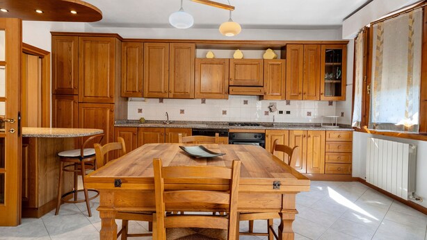 A spacious kitchen with wooden cabinets, a granite countertop, and a dining area with a wooden table and chairs. - Girasole Apartment – Comfort & Fast WiFi in the Heart of Valdarno (Pestello)