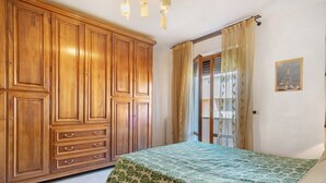 A bedroom with a large wooden wardrobe, a bed with a green leaf-patterned bedspread, and a window with curtains. - Girasole Apartment – Comfort & Fast WiFi in the Heart of Valdarno (Pestello)