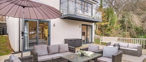 Un patio moderno al aire libre con un conjunto de sofá, una mesa y una sombrilla grande.