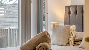 Una camera da letto con un'ampia finestra, un letto con cuscini, una lampada da comodino e vista su una recinzione in legno.