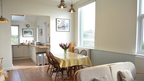A dining area with a table, chairs, and a sofa. There is a window with a view, a clock on the wall, and a radiator. - 3 Bed in Aberystwyth (oc-bow115) (Aberystwyth)