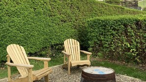 A house with a white exterior, two wooden Adirondack chairs, and a metal barrel on a gravel area. - 3 Bed in Aberystwyth (oc-bow115) (Aberystwyth)