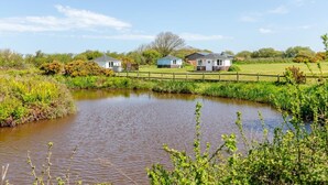 A pond with a wooden fence, houses in the background, and greenery around. - 1 Bed in Hartland (oc-h34690) (Hartland)