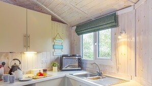 A compact kitchen with wooden cabinets, a built-in microwave, a sink, and a window with a view of greenery. - 1 Bed in Hartland (oc-h34690) (Hartland)