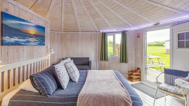 A cozy room with a wooden ceiling, a bed, a sofa, a painting, and a view of the outdoors. - 1 Bed in Hartland (oc-h34690) (Hartland)