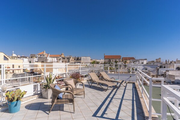 Terraza en la azotea con sillones de descanso, plantas en macetas y vistas panorámicas de la ciudad.
