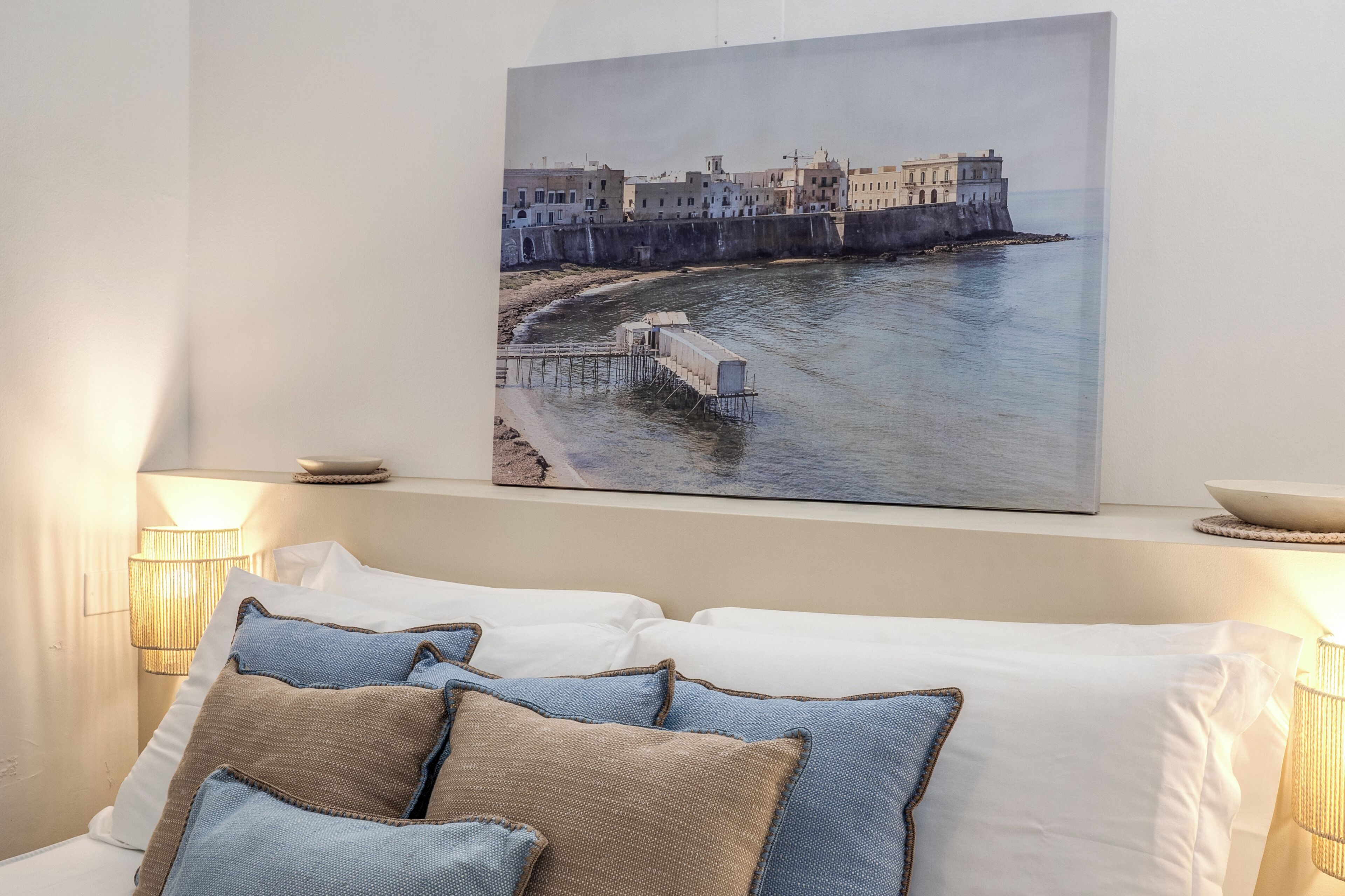 Ein Schlafzimmer mit einem Bett, Kissen, einem Wandbild mit einer Küstenansicht und Nachttischlampen.