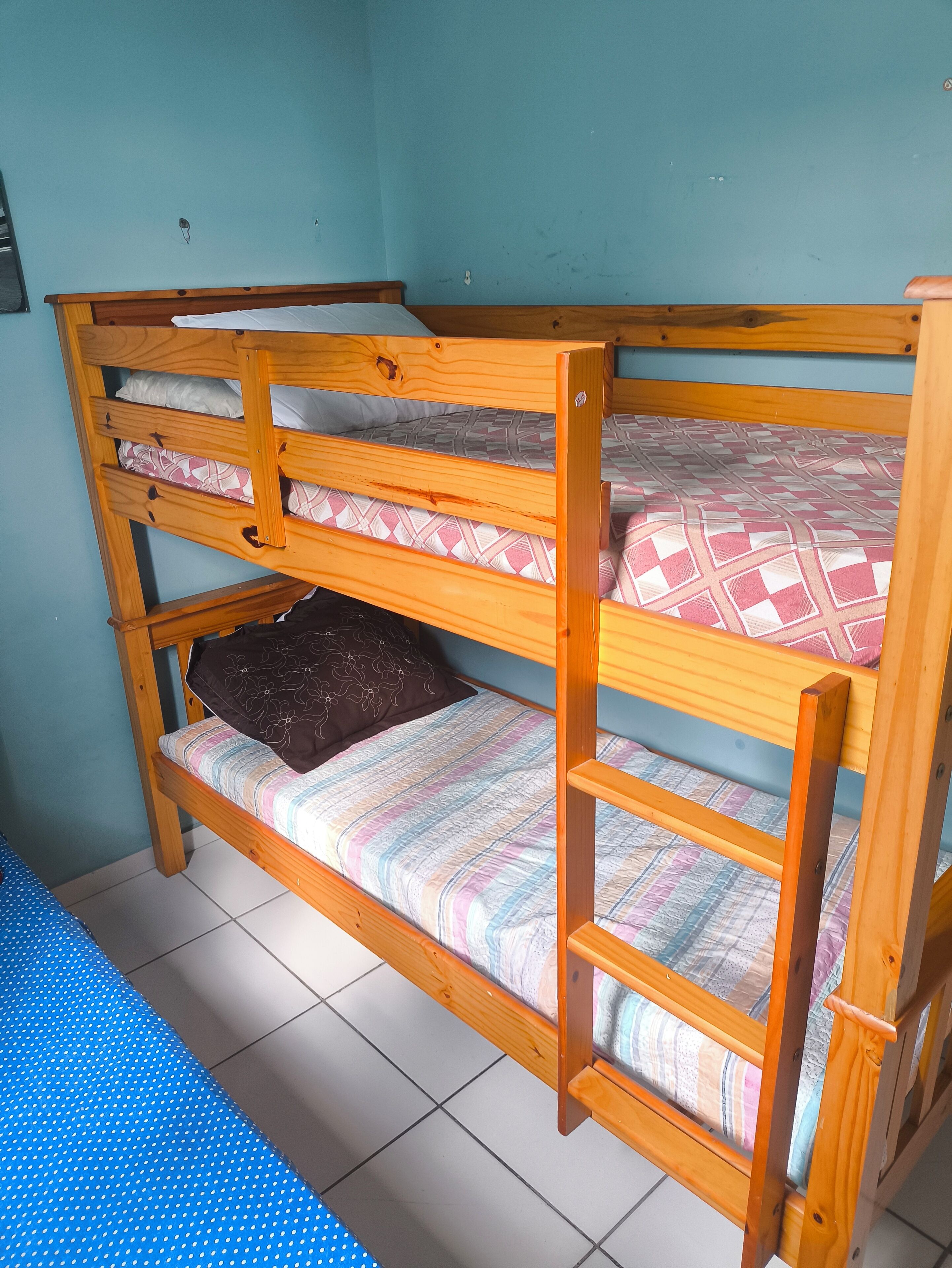 A bunk bed with a patterned mattress, a blue wall, and a tiled floor.