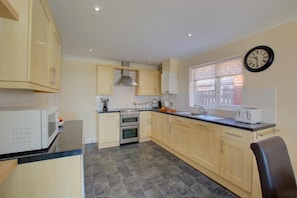 A modern kitchen with light wooden cabinets, a built-in oven, a microwave, and a window with patterned curtains. - 4 Bed in Bacton (oc-1990) (Bacton)