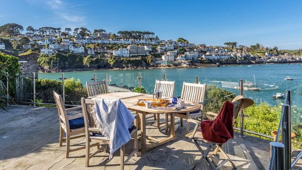 Eine Terrasse am Meer mit Tisch und Stühlen, mit Blick auf eine Küstenstadt und das Meer.