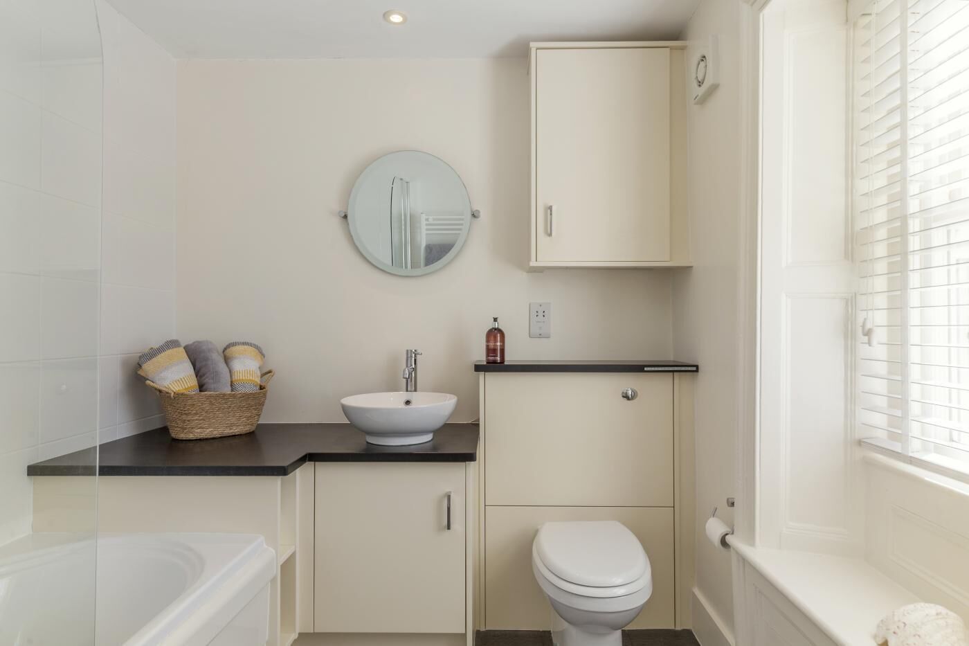 A bathroom with a white sink, a round mirror, a toilet, and a bathtub.