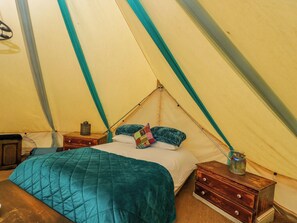 Ein Zelt mit Bett, Kissen, einer gesteppten Decke, einer hölzernen Kommode und einem kleinen Tisch mit einem Einmachglas.