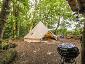 A tent set up in a forest with a grill nearby. - The Moroccan Bell Tent (Newbury)