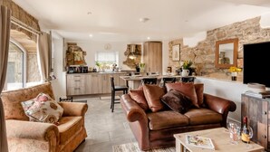 A cozy living room with a sofa, a coffee table with wine glasses, and a kitchen in the background. - 3 Bed in Gilsland (oc-f34699) (Waterhead)