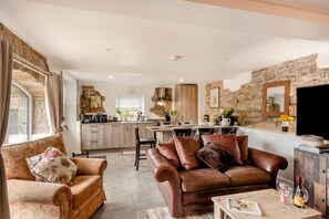 A cozy living room with a sofa, a coffee table with wine glasses, and a kitchen in the background. - 3 Bed in Gilsland (oc-f34699) (Waterhead)