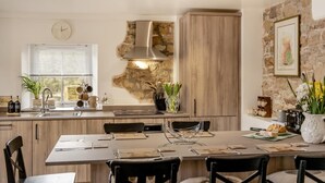 A modern kitchen with a stone accent wall, wooden cabinets, and a dining area with a table set for four. - 3 Bed in Gilsland (oc-f34699) (Waterhead)