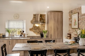 A modern kitchen with a stone accent wall, wooden cabinets, and a dining area with a table set for four. - 3 Bed in Gilsland (oc-f34699) (Waterhead)
