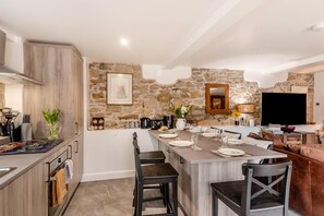 A modern kitchen with a stone accent wall, a dining area with a TV, and a cozy seating area. - 3 Bed in Gilsland (oc-f34699) (Waterhead)