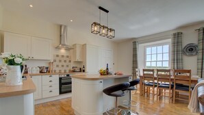 Una cocina moderna con armarios blancos, una isla central, taburetes de bar y un comedor con mesa y sillas.