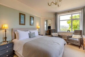 A hotel room with a large bed, two bedside tables, a desk, a chair, a mirror, and a window with a view.