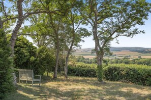 Un banc situé dans un espace verdoyant, agrémenté d’arbres, d’où l’on peut admirer un paysage rural.