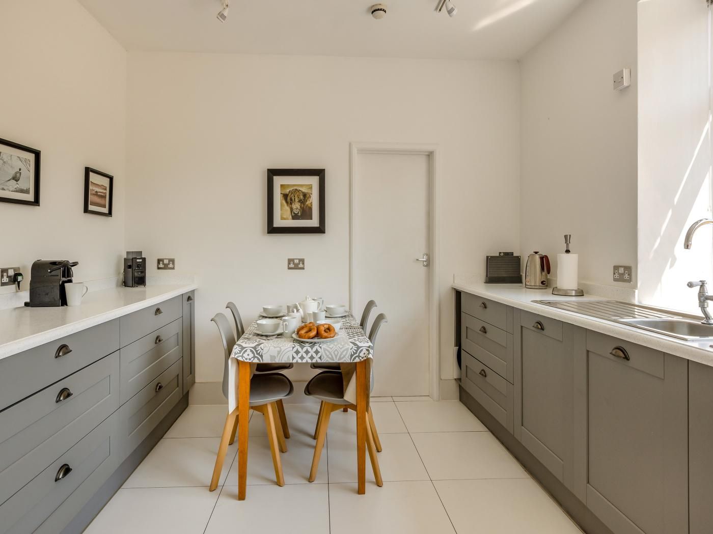 Una cocina compacta con una mesa de comedor, gabinetes grises y una cafetera.