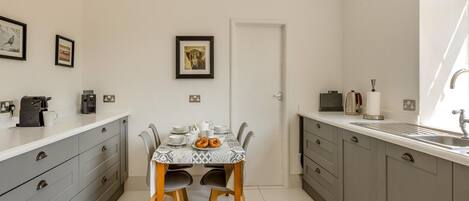 Una cocina compacta con una mesa de comedor, gabinetes grises y una cafetera.