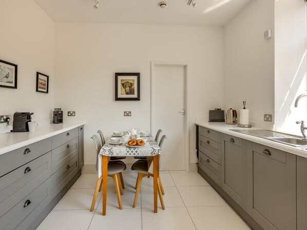 A compact kitchen with a dining table, grey cabinets, and a coffee machine.