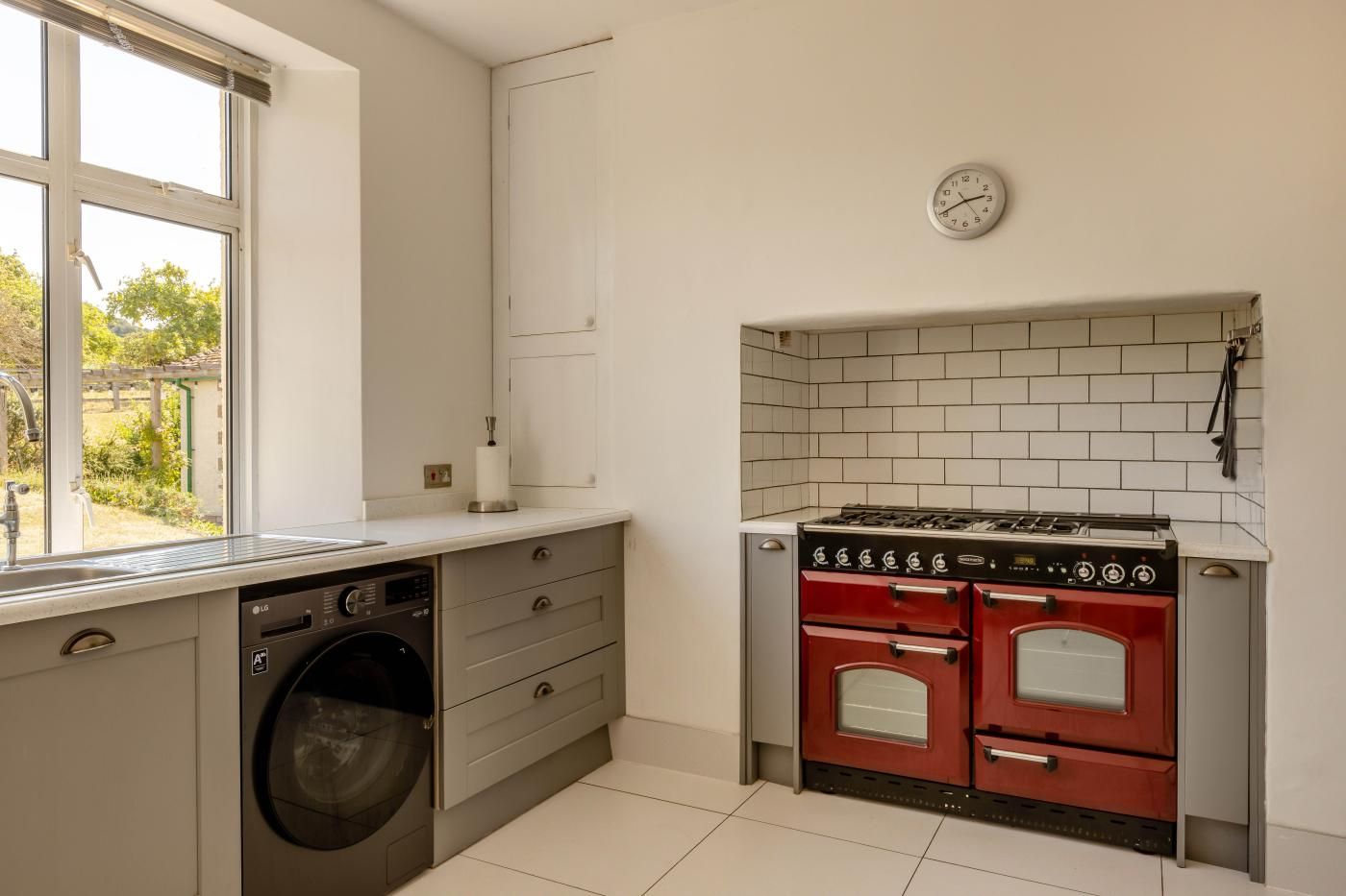 A compact kitchen with a washing machine, a red stove, and a clock on the wall.