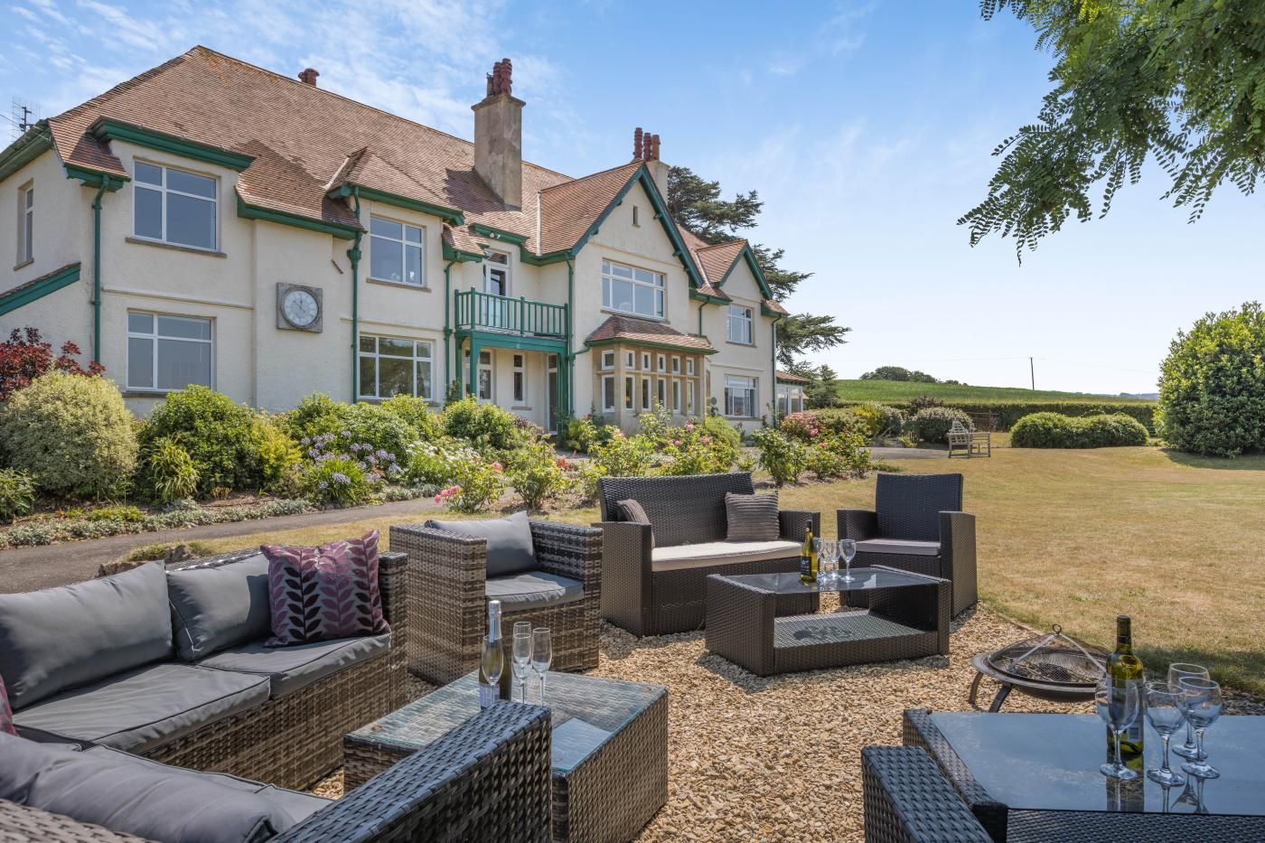 A large house with a garden patio featuring wicker furniture and outdoor seating.