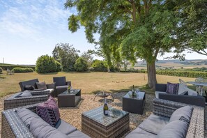 An outdoor seating area with wicker furniture, a table with a bottle and glasses, and a view of the countryside.