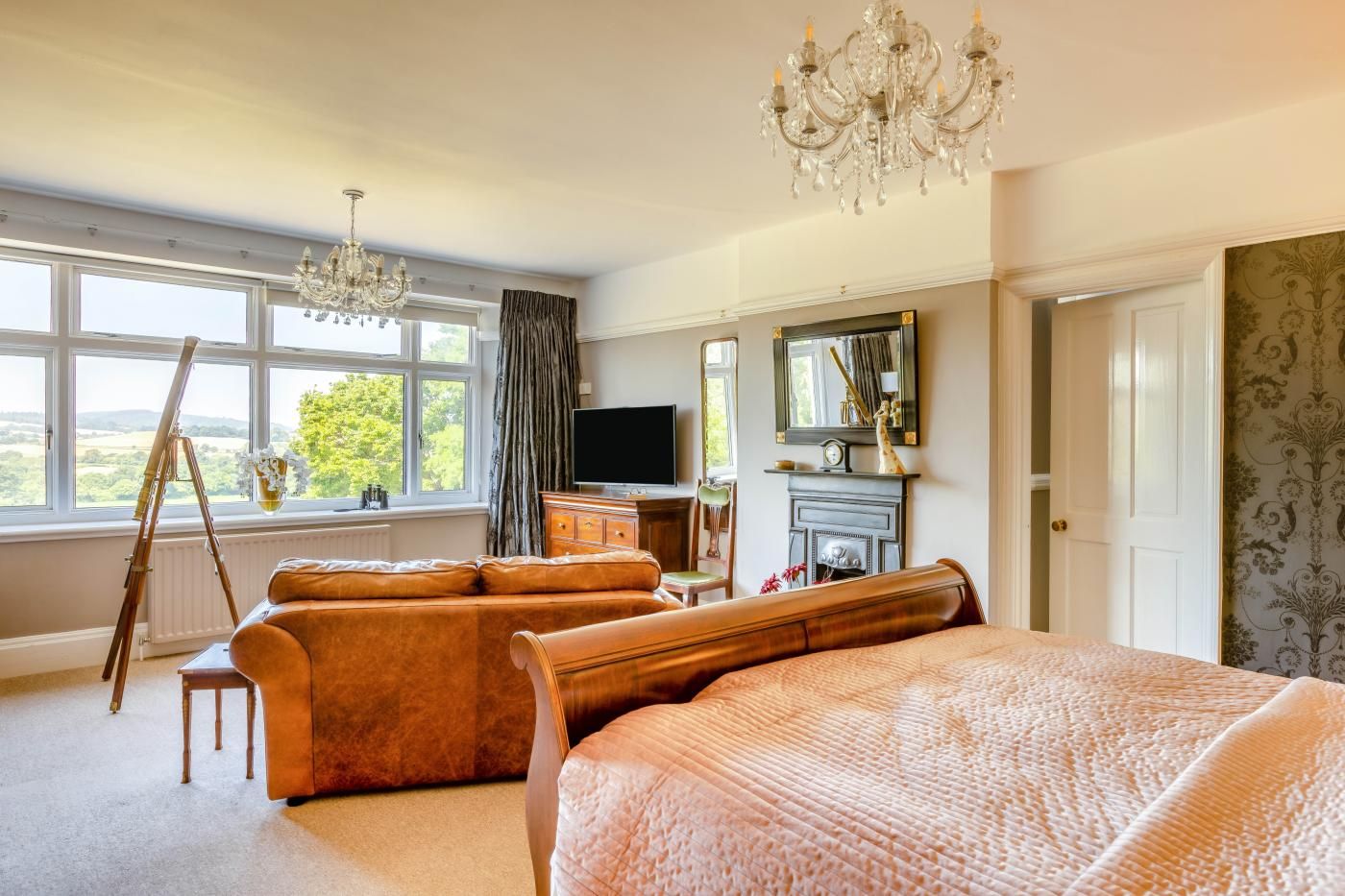 A spacious bedroom with a large bed, a sitting area with a sofa and armchair, a television, and a fireplace.