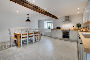A modern kitchen with white cabinetry, a wooden dining table, and a large window. - 4 Bed in Ruthin (oc-bow136) (Gwyddelwern)