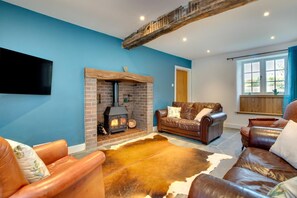 A living room with a brick fireplace, leather sofas, a cowhide rug, and a television mounted on the wall. - 4 Bed in Ruthin (oc-bow136) (Gwyddelwern)