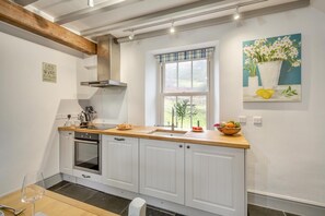 A kitchen with white cabinets, a stainless steel range hood, a window with a view, and a painting on the wall.