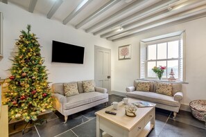 A living room with a Christmas tree, two sofas, a coffee table, a flat-screen TV, and a window with a view. - 3 Bed in Islawrdref (oc-t34600) (Islawr-dref)