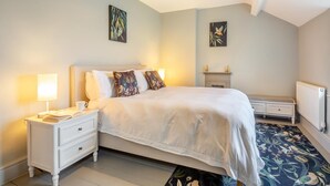 Ein Schlafzimmer mit Bett, Nachttischen, einer Lampe, einem Kamin und Bildern an den Wänden.